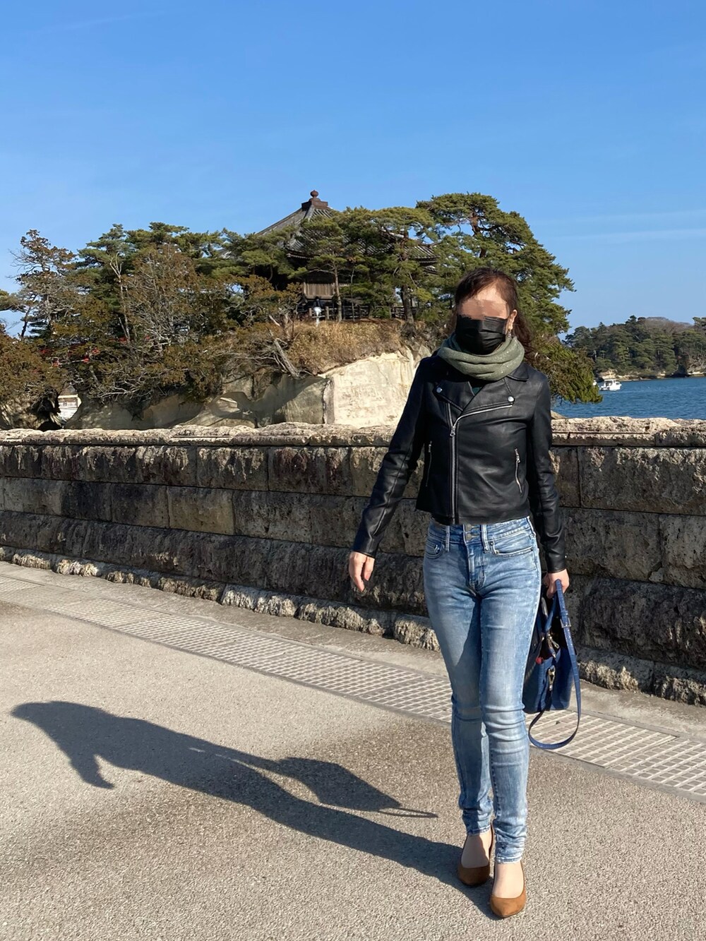 ブルー系のデニムパンツ、ブラック系のライダースジャケット、ブルー系のトートバッグを着用したレディースの春コーディネートの2枚目の写真