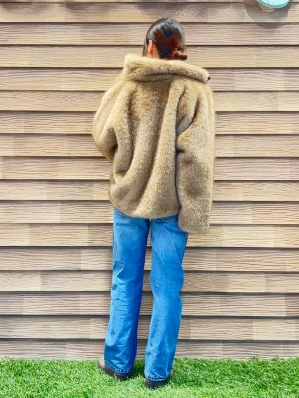 イエロー系のブルゾン、ベージュ系のニット/セーター、ブルー系のデニムパンツを着用したレディースの冬コーディネートの3枚目の写真