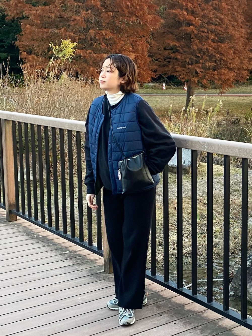 グレー系のスニーカー、ブルー系のダウンベスト、ブラック系のショルダーバッグを着用したレディースの冬コーディネートの2枚目の写真