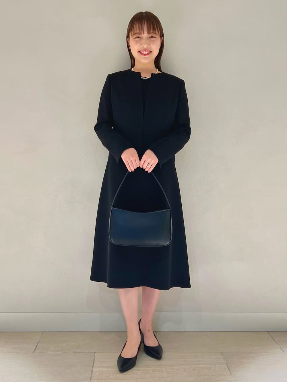 ブルー系のノーカラージャケット、ブルー系のワンピース、ブラック系のハンドバッグを着用したレディースの冬コーディネートの2枚目の写真