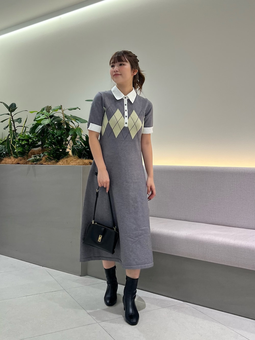 グレー系のワンピース、ブラック系のブーツ、ブラック系のショルダーバッグを着用したレディースの秋コーディネートの2枚目の写真