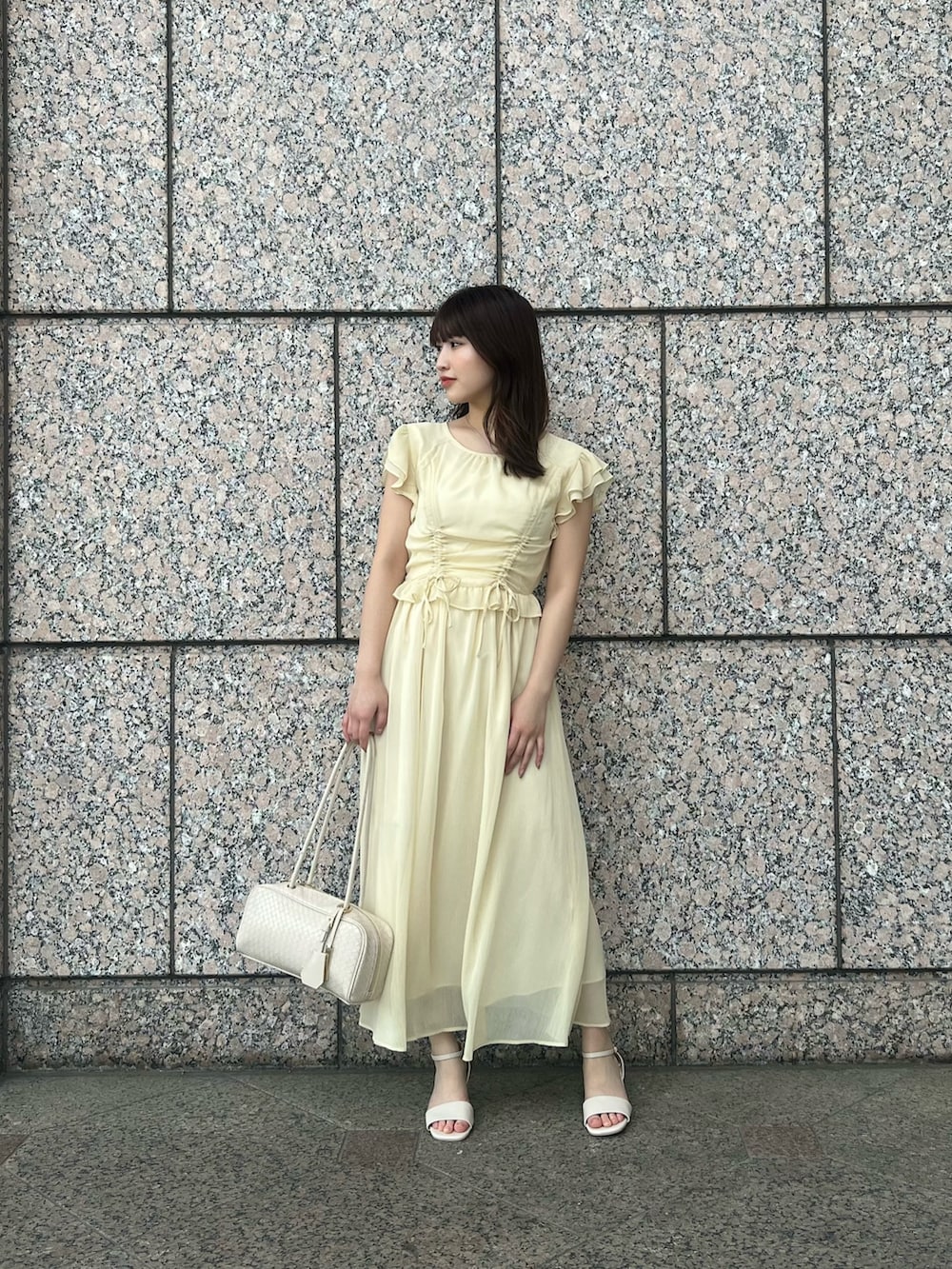 イエロー系のワンピース、ホワイト系のボストンバッグ、ホワイト系のサンダルを着用したレディースの夏コーディネートの2枚目の写真