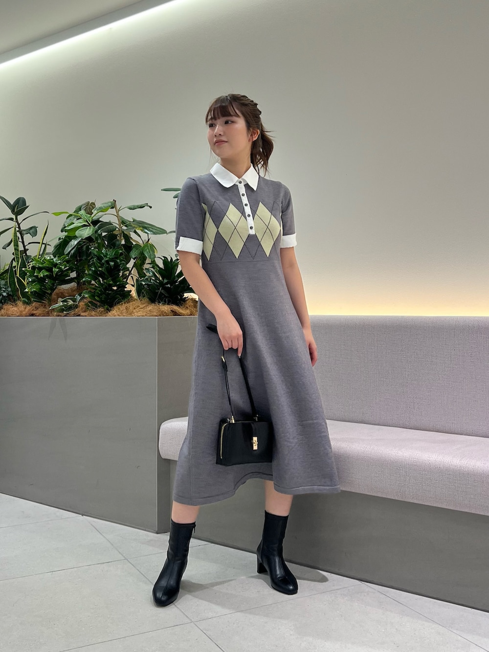 グレー系のワンピース、ブラック系のブーツ、ブラック系のショルダーバッグを着用したレディースの秋コーディネートの4枚目の写真