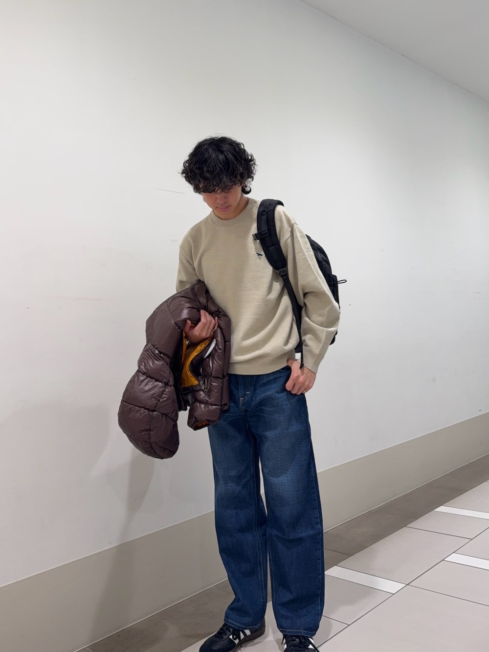 ブラウン系のダウンジャケット/コート、ホワイト系のニット/セーター、ブルー系のデニムパンツを着用したメンズの冬コーディネートの4枚目の写真