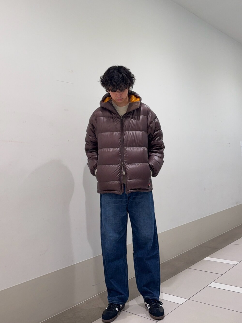 ブラウン系のダウンジャケット/コート、ホワイト系のニット/セーター、ブルー系のデニムパンツを着用したメンズの冬コーディネートの2枚目の写真