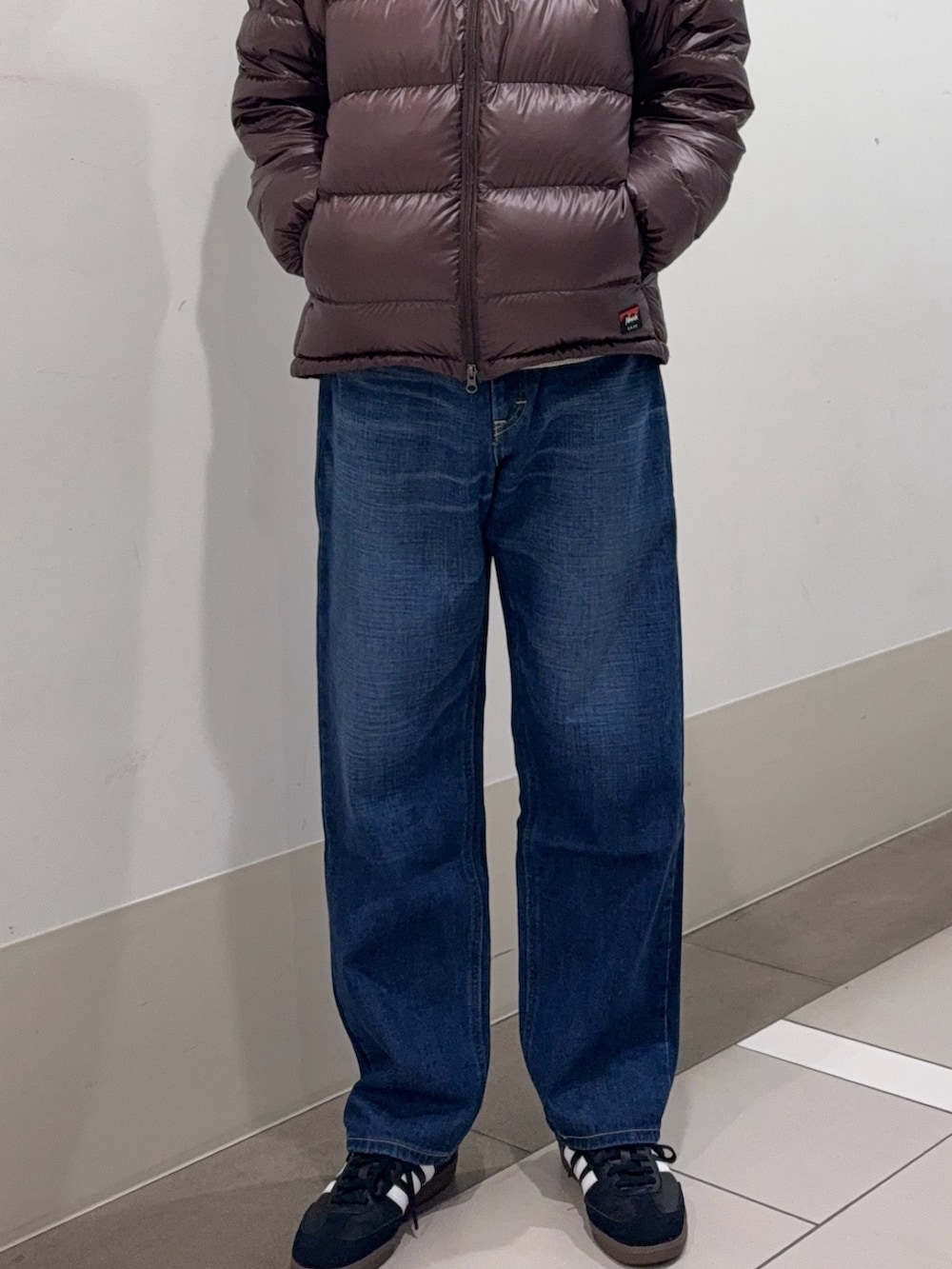 ブラウン系のダウンジャケット/コート、ホワイト系のニット/セーター、ブルー系のデニムパンツを着用したメンズの冬コーディネートの5枚目の写真