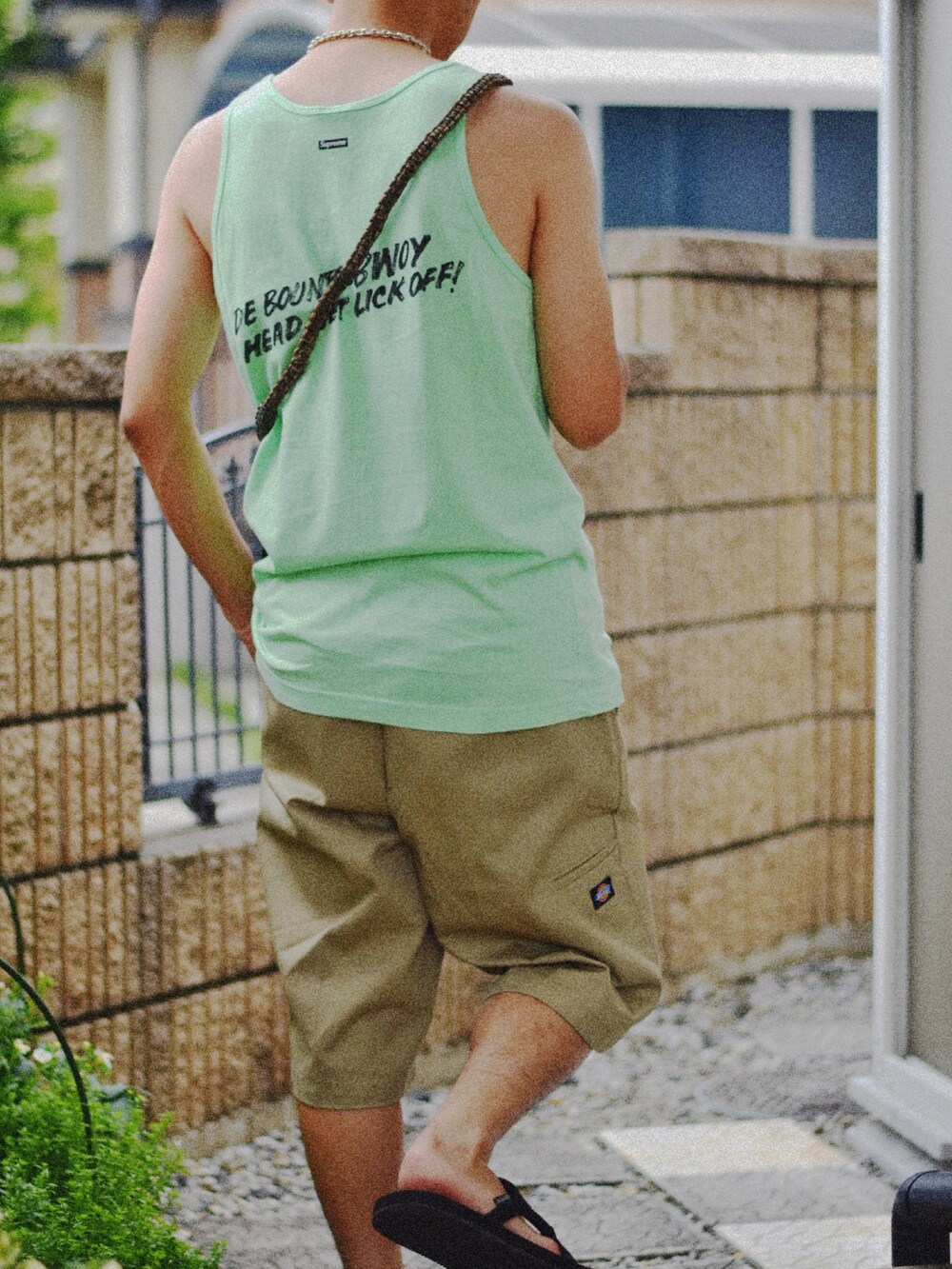 ベージュ系のチノパンツ、ブラック系のサンダル、グリーン系のタンクトップを着用したメンズの夏コーディネートの2枚目の写真