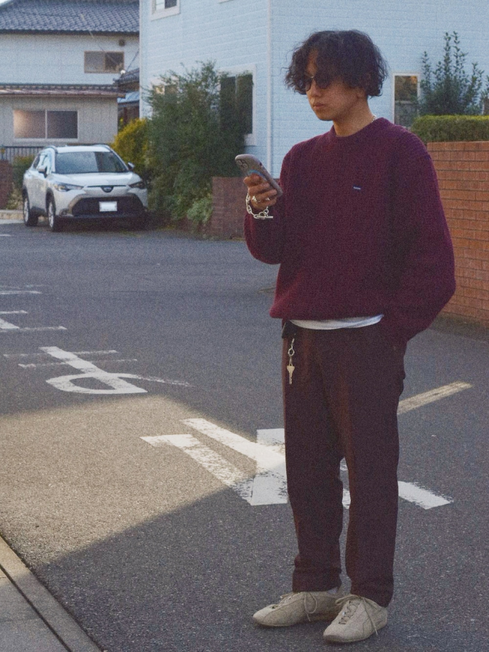 レッド系のニット/セーター、ブラウン系のスラックス、シルバー系のブレスレットを着用したメンズの秋コーディネートの2枚目の写真