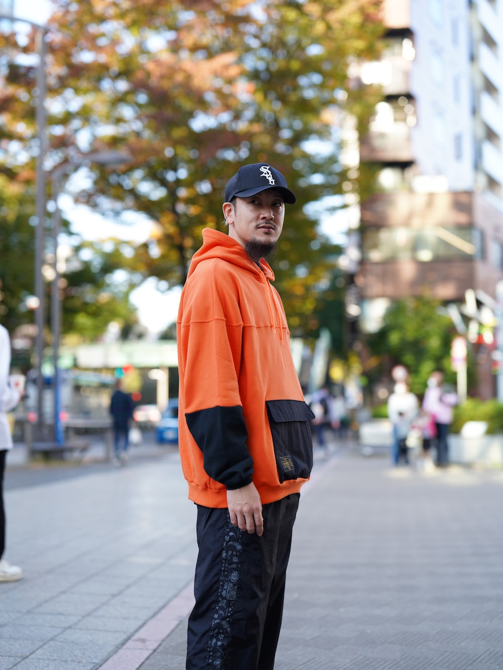 オレンジ系のパーカー、ブラック系のその他パンツ、ブラック系のキャップを着用したメンズの秋コーディネートの3枚目の写真