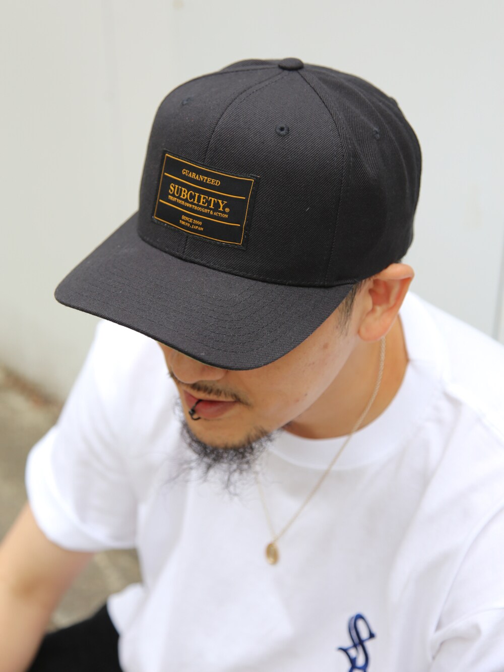 ホワイト系のTシャツ/カットソー、ブラック系のスラックス、ブラック系のキャップを着用したメンズの夏コーディネートの3枚目の写真