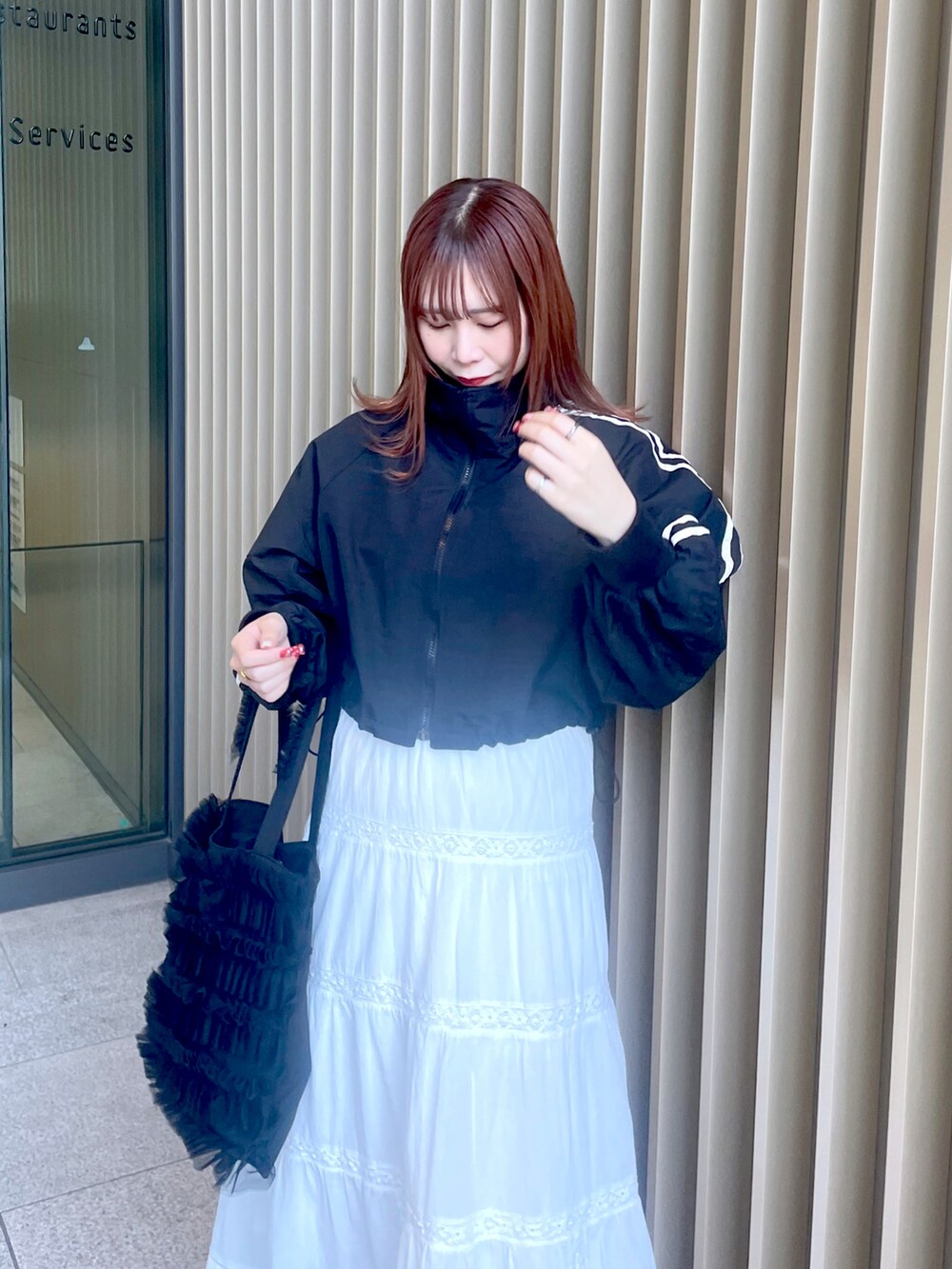 ホワイト系のスカート、ブラック系のスニーカー、ブラック系のトートバッグを着用したレディースの春コーディネートの2枚目の写真