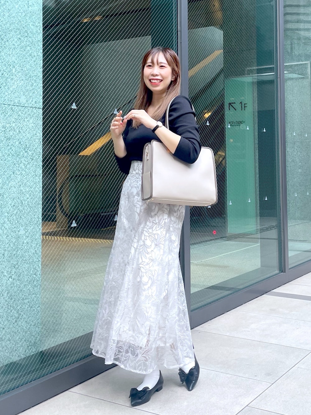 ブラック系のパンプス、ホワイト系のスカート、ベージュ系のショルダーバッグを着用したレディースの夏コーディネートの2枚目の写真
