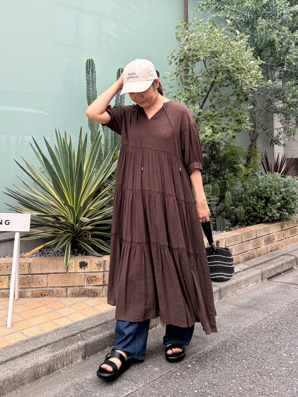ブラウン系のワンピース、ブラック系のサンダル、ベージュ系のキャップを着用したレディースの夏コーディネートの2枚目の写真