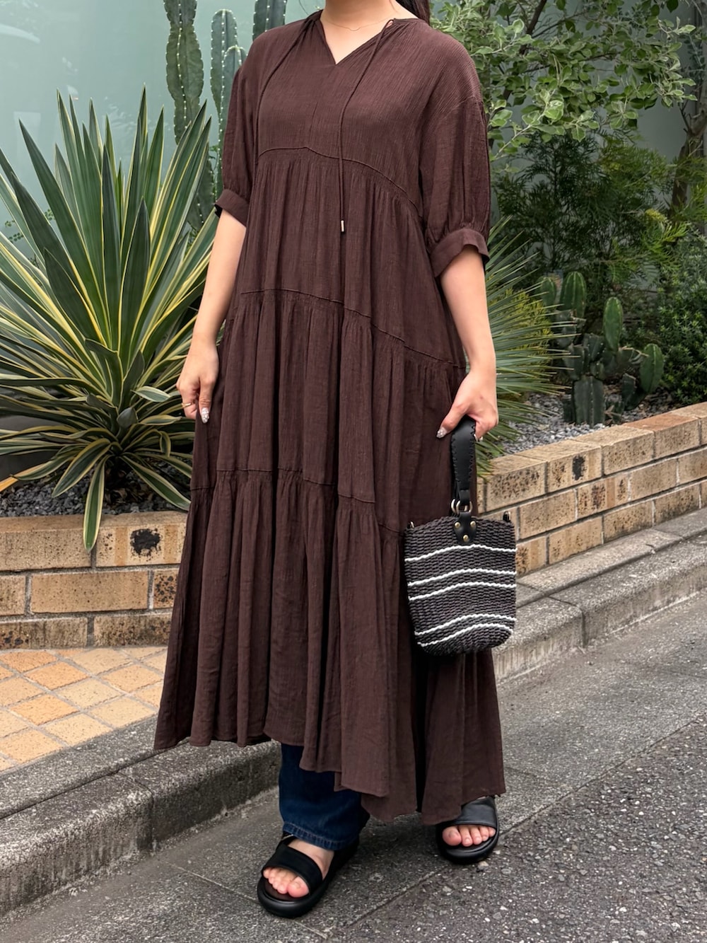 ブラウン系のワンピース、ブラック系のサンダル、ベージュ系のキャップを着用したレディースの夏コーディネートの3枚目の写真