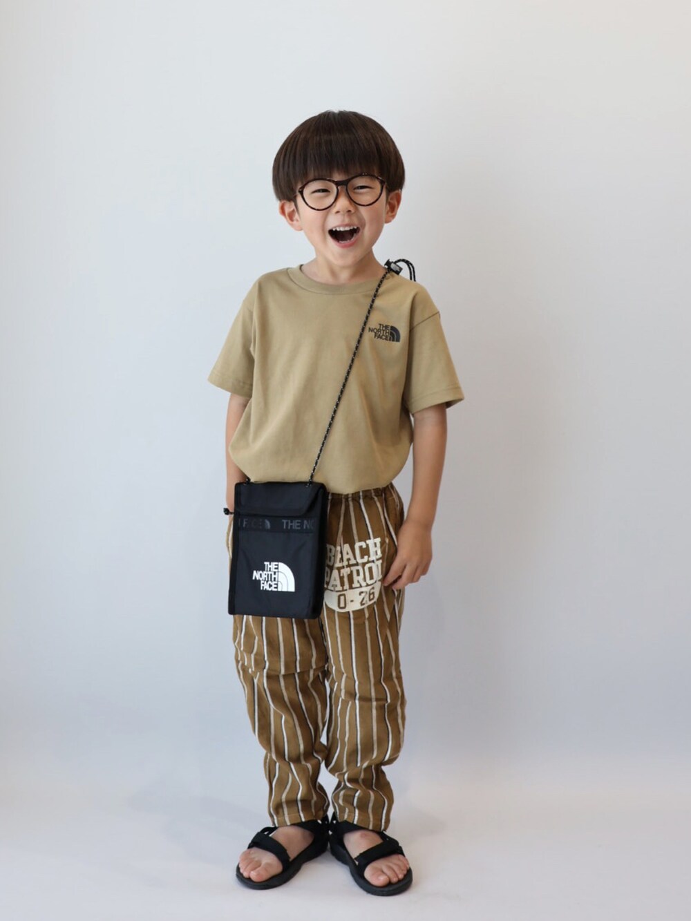 ベージュ系のTシャツ/カットソー、ブラウン系のパンツ、ブラック系のサンダルを着用したキッズの夏コーディネートの2枚目の写真