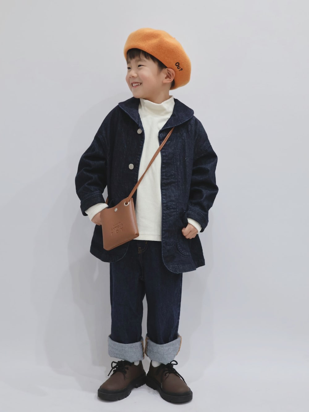 ブルー系のカバーオール、ブラウン系のショルダーバッグ、ホワイト系のトップスを着用したキッズの冬コーディネートの4枚目の写真