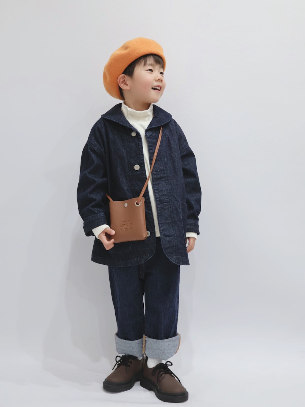 ブルー系のカバーオール、ブラウン系のショルダーバッグ、ホワイト系のトップスを着用したキッズの冬コーディネートの5枚目の写真