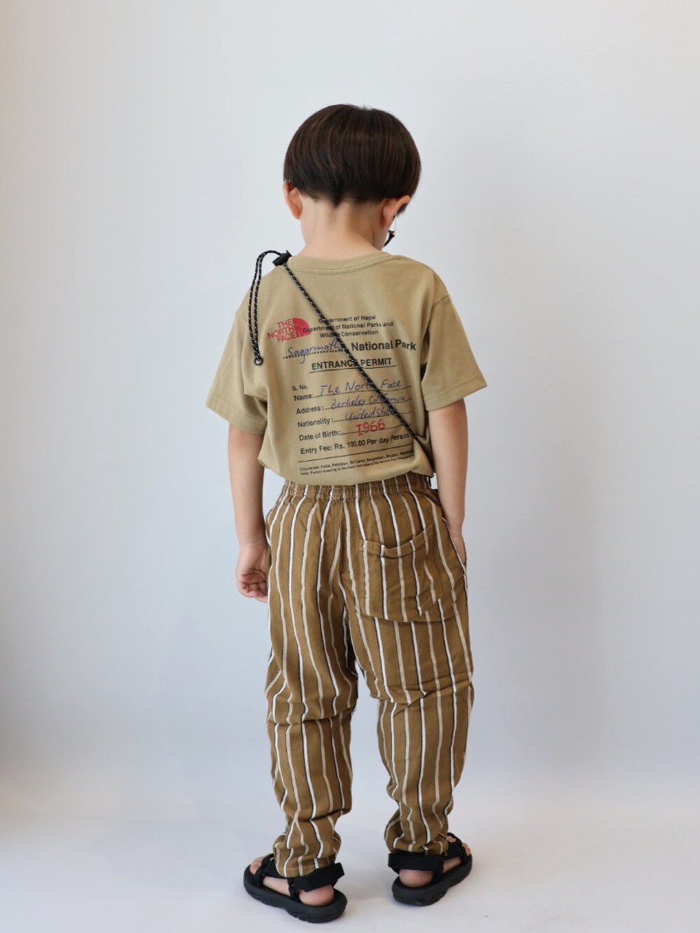 ベージュ系のTシャツ/カットソー、ブラウン系のパンツ、ブラック系のサンダルを着用したキッズの夏コーディネートの3枚目の写真