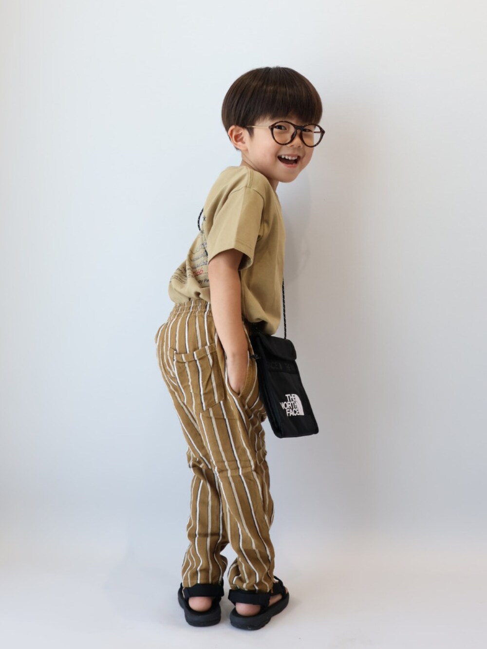 ベージュ系のTシャツ/カットソー、ブラウン系のパンツ、ブラック系のサンダルを着用したキッズの夏コーディネートの4枚目の写真