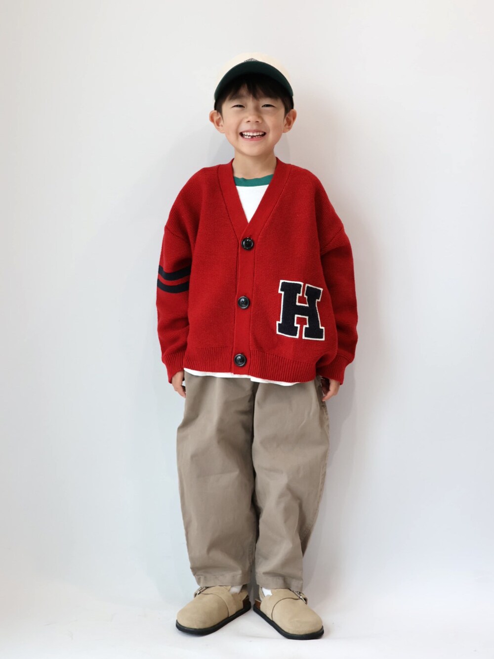 レッド系のカーディガン/ボレロ、グリーン系のTシャツ/カットソー、ブラウン系のチノパンツを着用したキッズの秋コーディネートの2枚目の写真