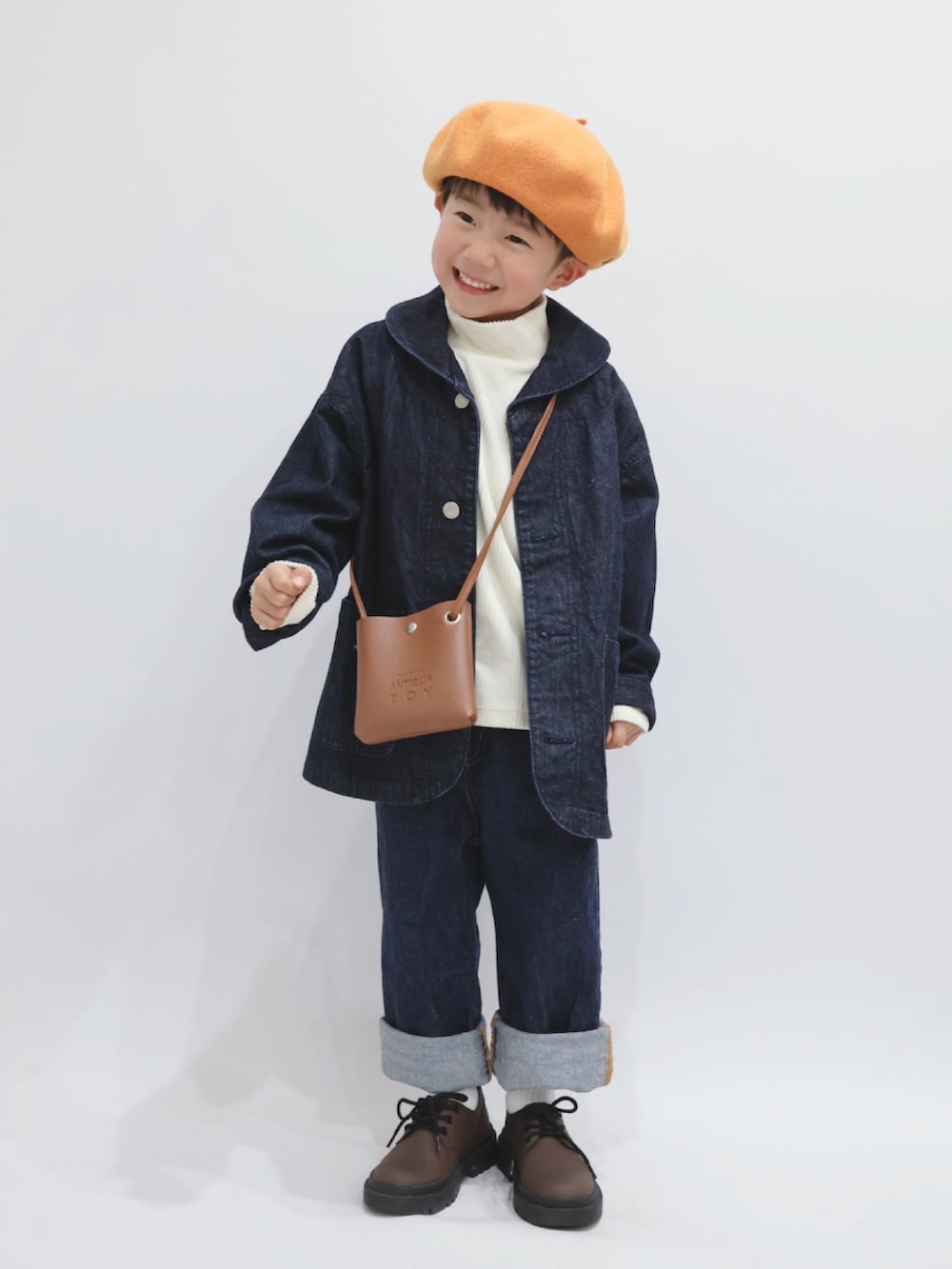 ブルー系のカバーオール、ブラウン系のショルダーバッグ、ホワイト系のトップスを着用したキッズの冬コーディネートの2枚目の写真