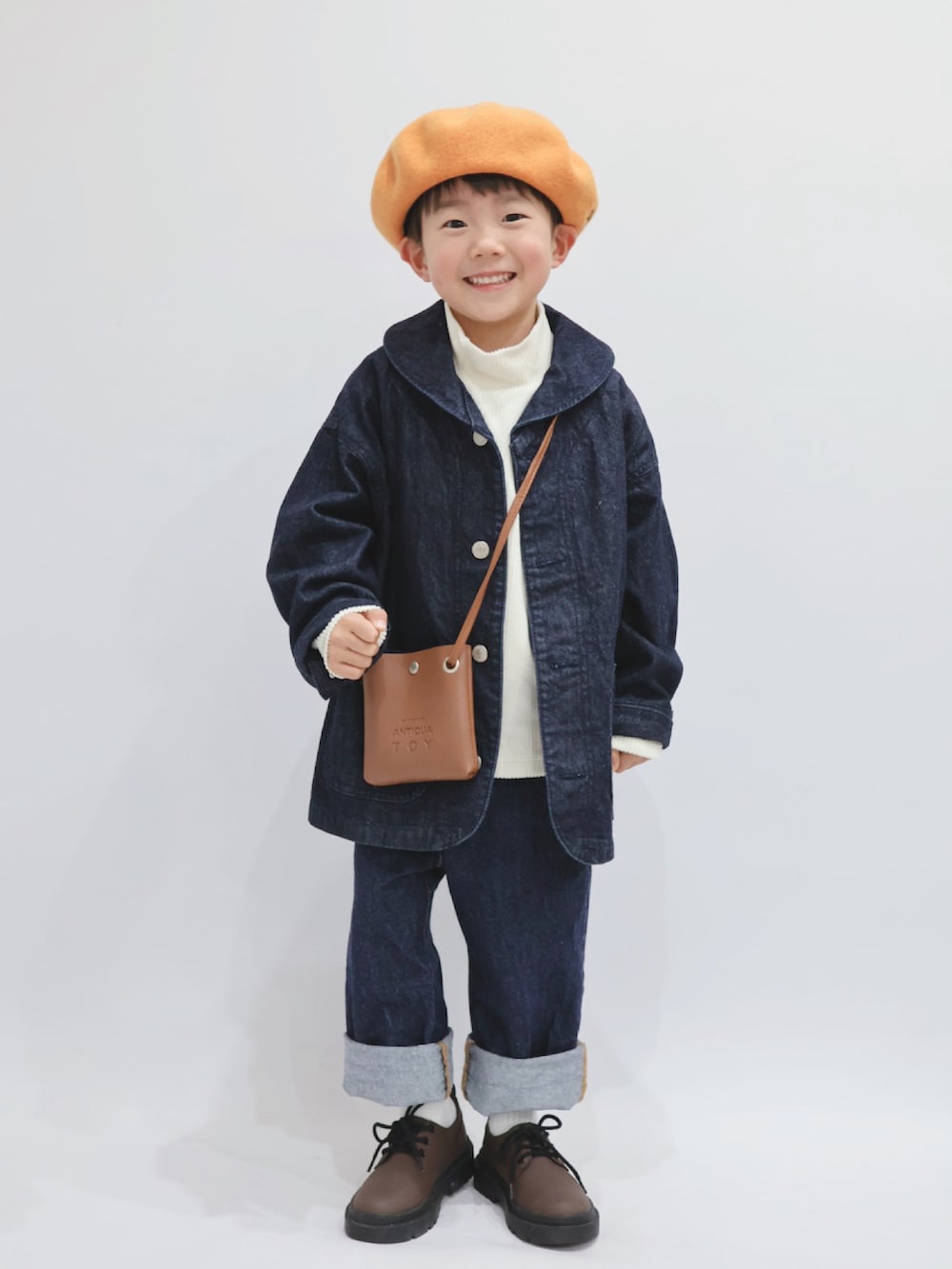 ブルー系のカバーオール、ブラウン系のショルダーバッグ、ホワイト系のトップスを着用したキッズの冬コーディネートの3枚目の写真