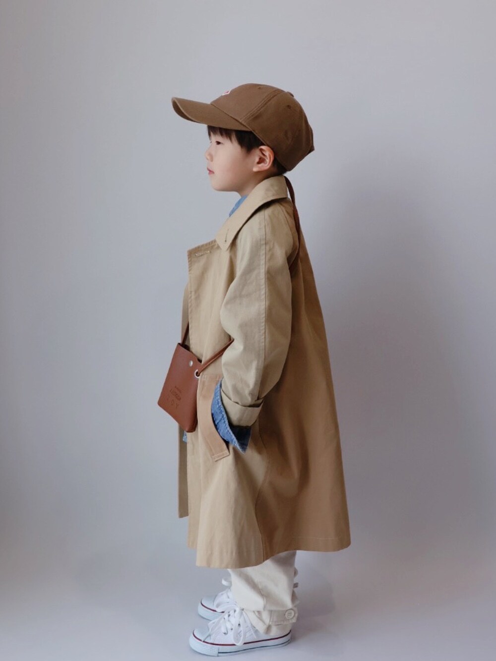 ベージュ系のステンカラーコート、ブラウン系のショルダーバッグ、ブルー系のシャツ/ブラウスを着用したキッズの春コーディネートの4枚目の写真