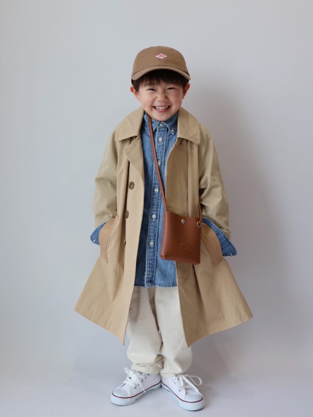 ベージュ系のステンカラーコート、ブラウン系のショルダーバッグ、ブルー系のシャツ/ブラウスを着用したキッズの春コーディネートの2枚目の写真