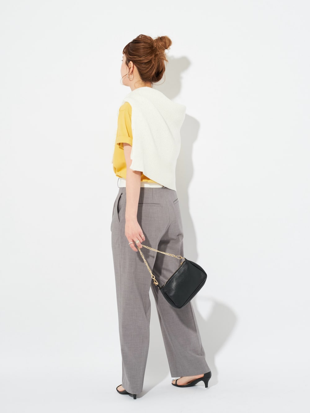 イエロー系のTシャツ/カットソー、ホワイト系のニット/セーター、グレー系のスラックスを着用したレディースの春コーディネートの3枚目の写真