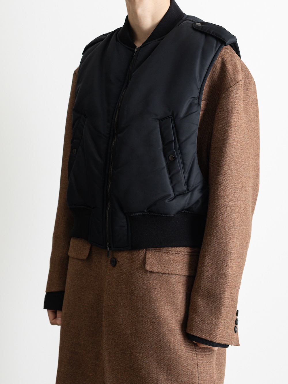 ブラック系のダウンベスト、ブラウン系のノーカラージャケット、ブラック系のその他パンツを着用したメンズの冬コーディネートの2枚目の写真