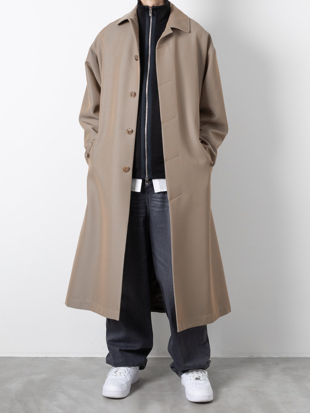 ブラック系のデニムパンツ、ブラック系のニット/セーター、ベージュ系のステンカラーコートを着用したメンズの秋コーディネートの3枚目の写真