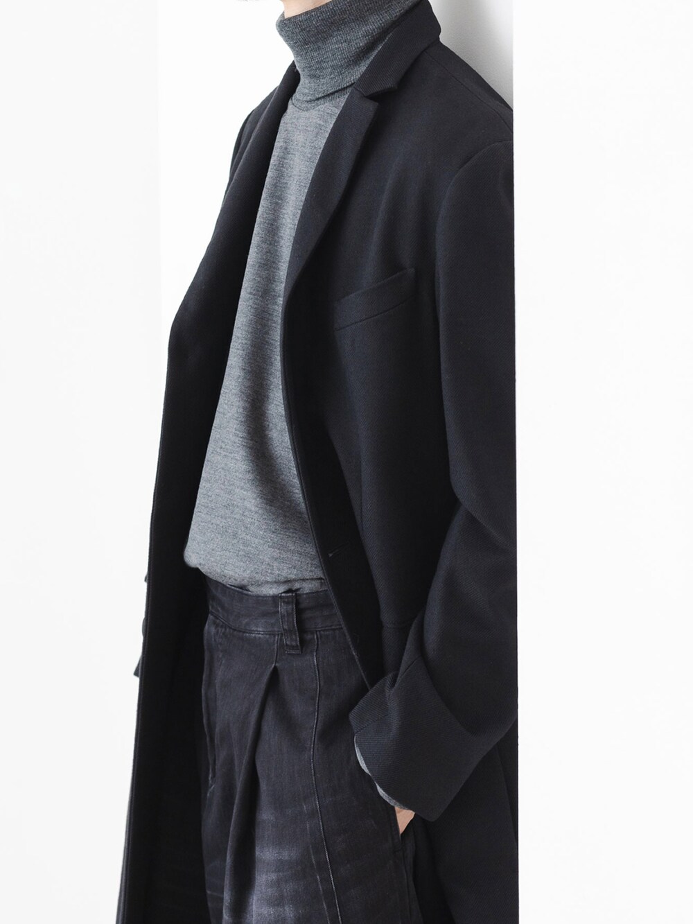 ブラック系のデニムパンツ、ブラック系のチェスターコート、グレー系のニット/セーターを着用したメンズの秋コーディネートの3枚目の写真