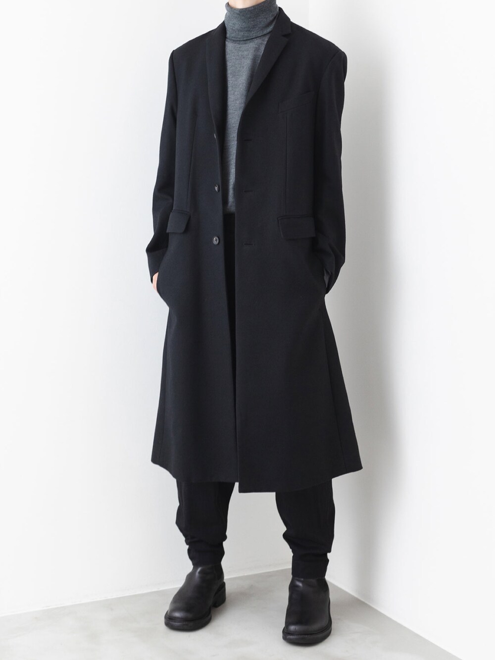 ブラック系のデニムパンツ、ブラック系のチェスターコート、グレー系のニット/セーターを着用したメンズの秋コーディネートの2枚目の写真