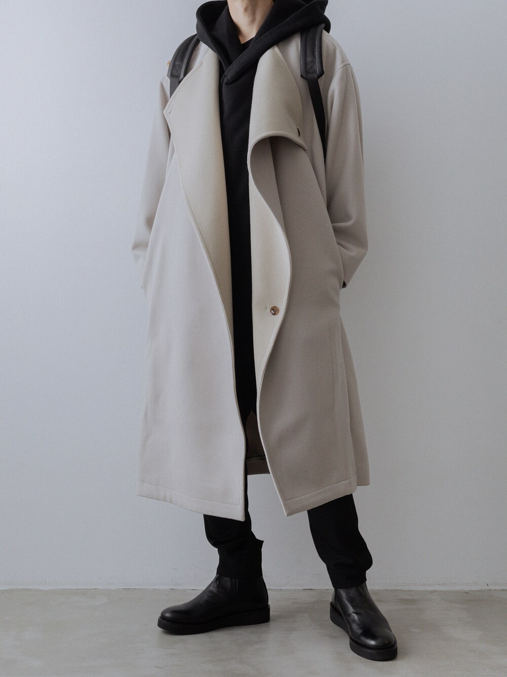 ホワイト系のチェスターコート、ブラック系のパーカー、ブラック系のその他パンツを着用したメンズの秋コーディネートの4枚目の写真