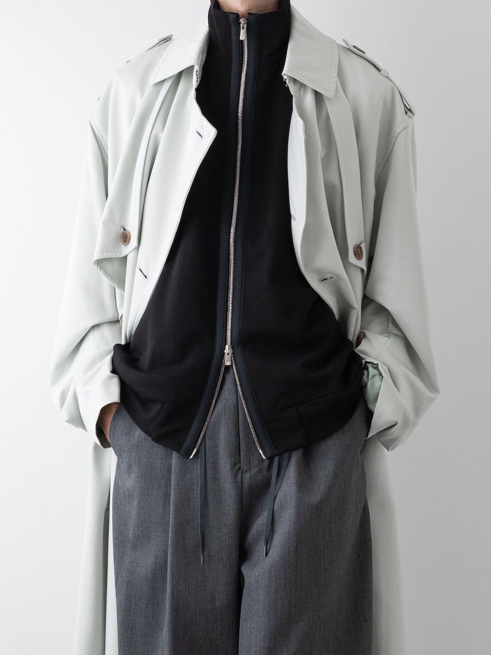 グレー系のその他パンツ、ブラック系のニット/セーター、グリーン系のトレンチコートを着用したメンズの秋コーディネートの2枚目の写真