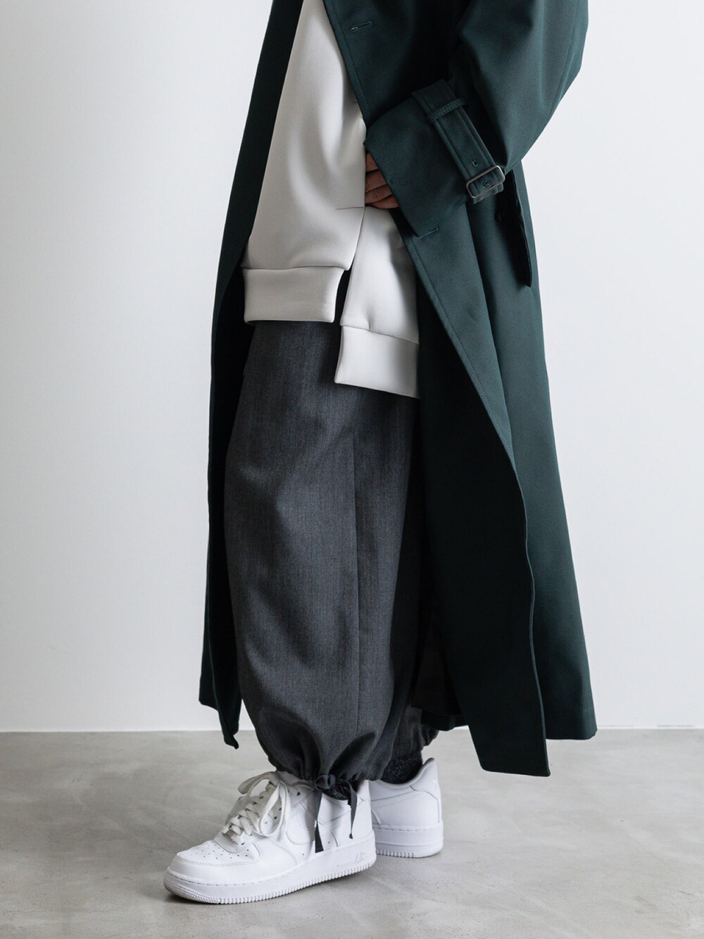 グレー系のその他パンツ、グレー系のTシャツ/カットソー、グリーン系のトレンチコートを着用したメンズの冬コーディネートの3枚目の写真