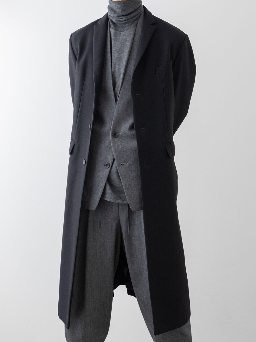 グレー系のノーカラージャケット、グレー系のニット/セーター、ブラック系のチェスターコートを着用したメンズの秋コーディネートの2枚目の写真