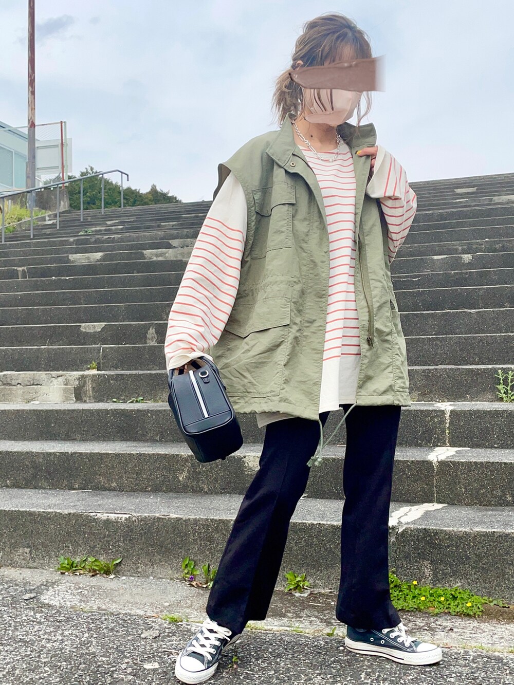 グリーン系のベスト、ブラック系のパンツ、オレンジ系のTシャツ/カットソーを着用したレディースの春コーディネートの3枚目の写真