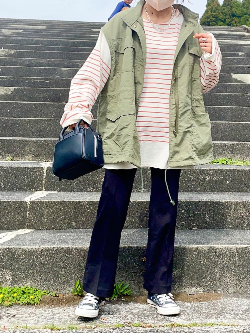 グリーン系のベスト、ブラック系のパンツ、オレンジ系のTシャツ/カットソーを着用したレディースの春コーディネートの4枚目の写真