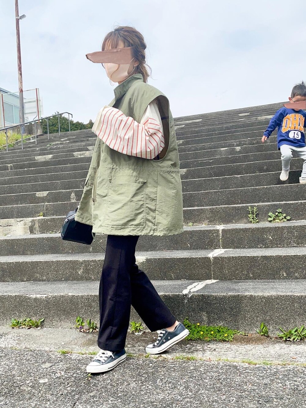 グリーン系のベスト、ブラック系のパンツ、オレンジ系のTシャツ/カットソーを着用したレディースの春コーディネートの2枚目の写真