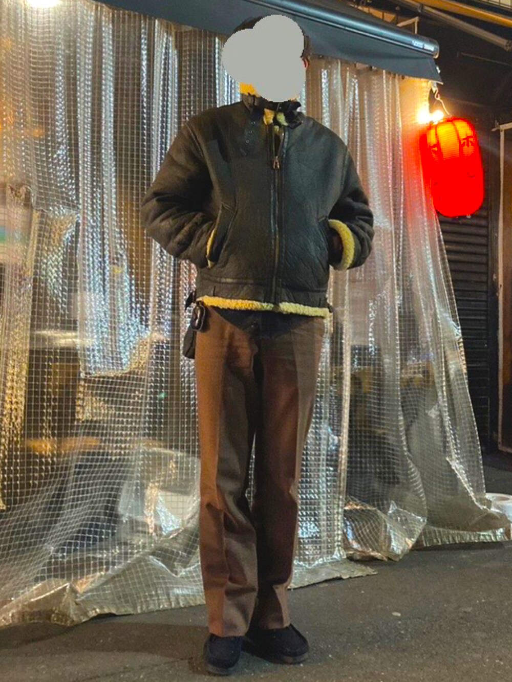 ブラック系のムートンコート、ブラウン系のスラックス、ブラック系のブーツを着用したメンズの春コーディネートの2枚目の写真