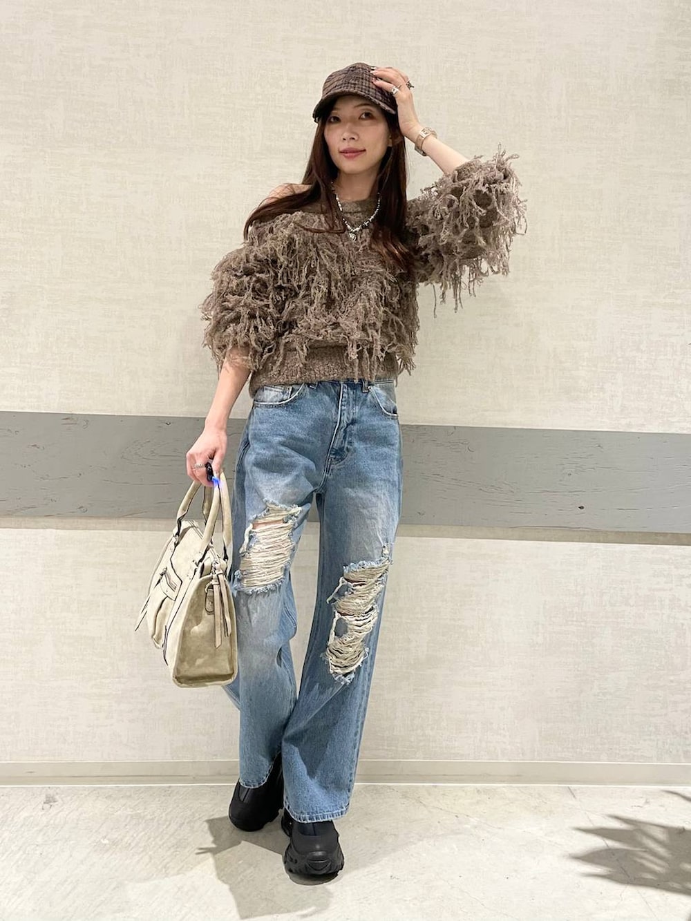 ベージュ系のボストンバッグ、ブラック系のブーツ、ブルー系のデニムパンツを着用したレディースの秋コーディネートの2枚目の写真