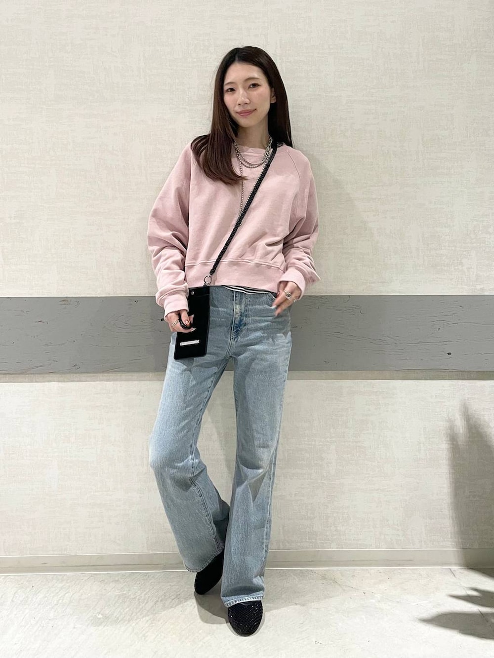 ブラック系のパンプス、ピンク系のスウェット、ブルー系のデニムパンツを着用したレディースの冬コーディネートの2枚目の写真