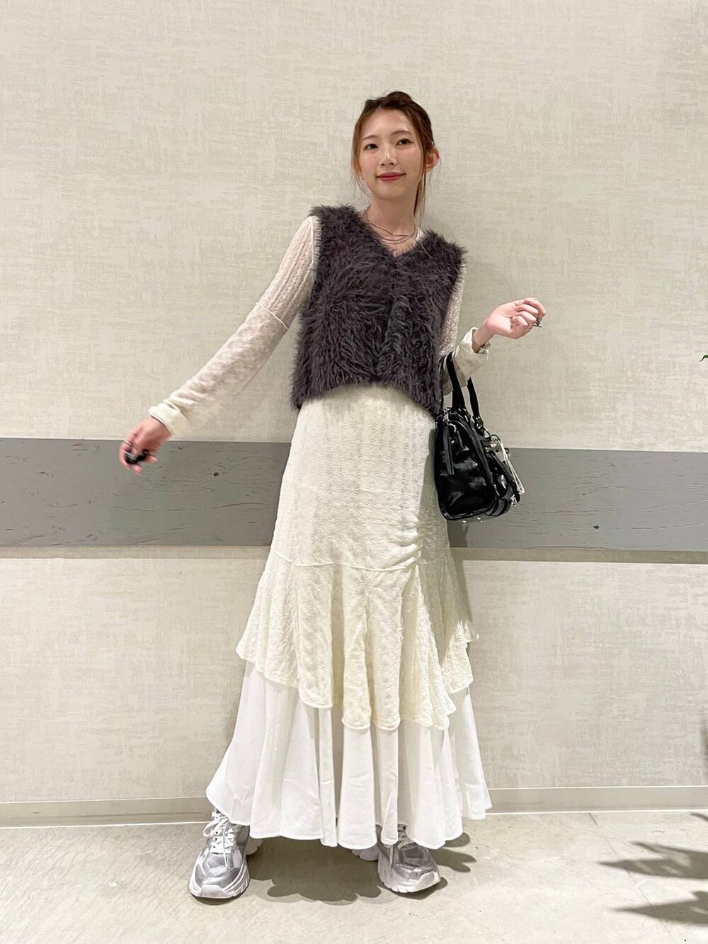 グレー系のベスト、ブラック系のボストンバッグ、シルバー系のスニーカーを着用したレディースの秋コーディネートの2枚目の写真