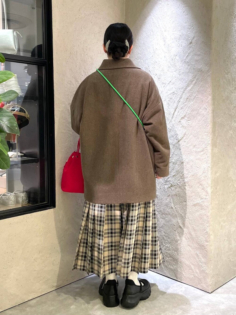 ブラウン系のチェスターコート、ブラック系のスニーカー、レッド系のハンドバッグを着用したレディースの秋コーディネートの3枚目の写真