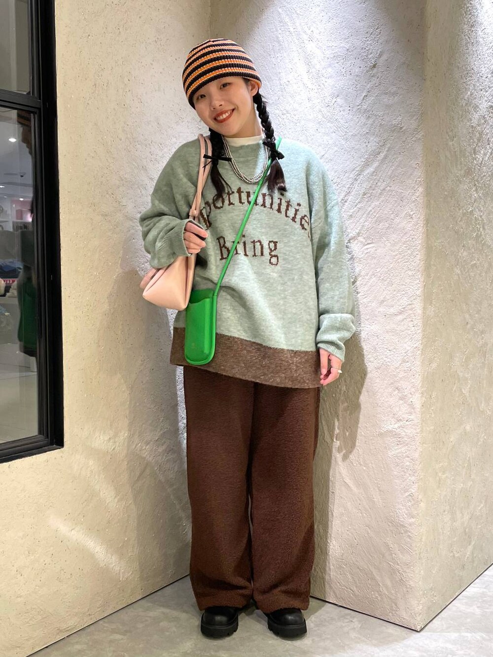 ブラック系のブーツ、ピンク系のショルダーバッグ、グリーン系のニット/セーターを着用したレディースの冬コーディネートの2枚目の写真