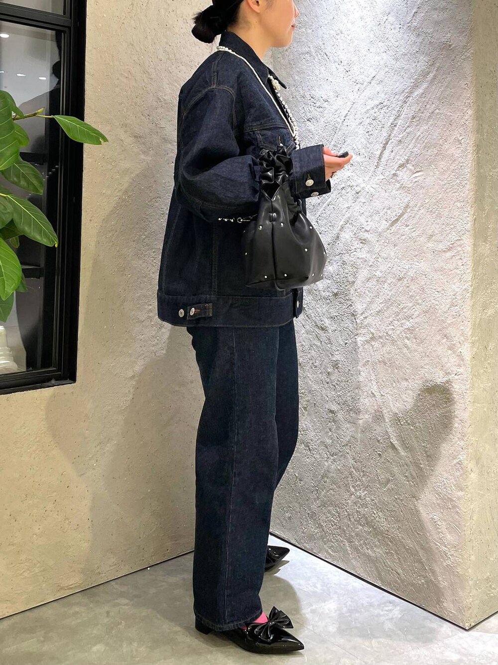 ブラック系のハンドバッグ、ブルー系のデニムパンツ、ブラック系のパンプスを着用したレディースの春コーディネートの6枚目の写真