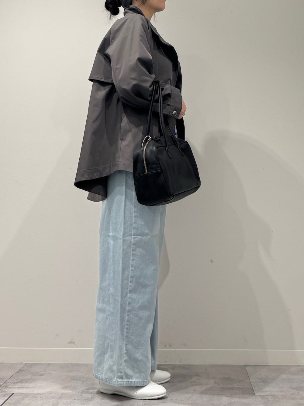 グレー系のトレンチコート、ブラック系のボストンバッグ、ブルー系のデニムパンツを着用したレディースの冬コーディネートの2枚目の写真