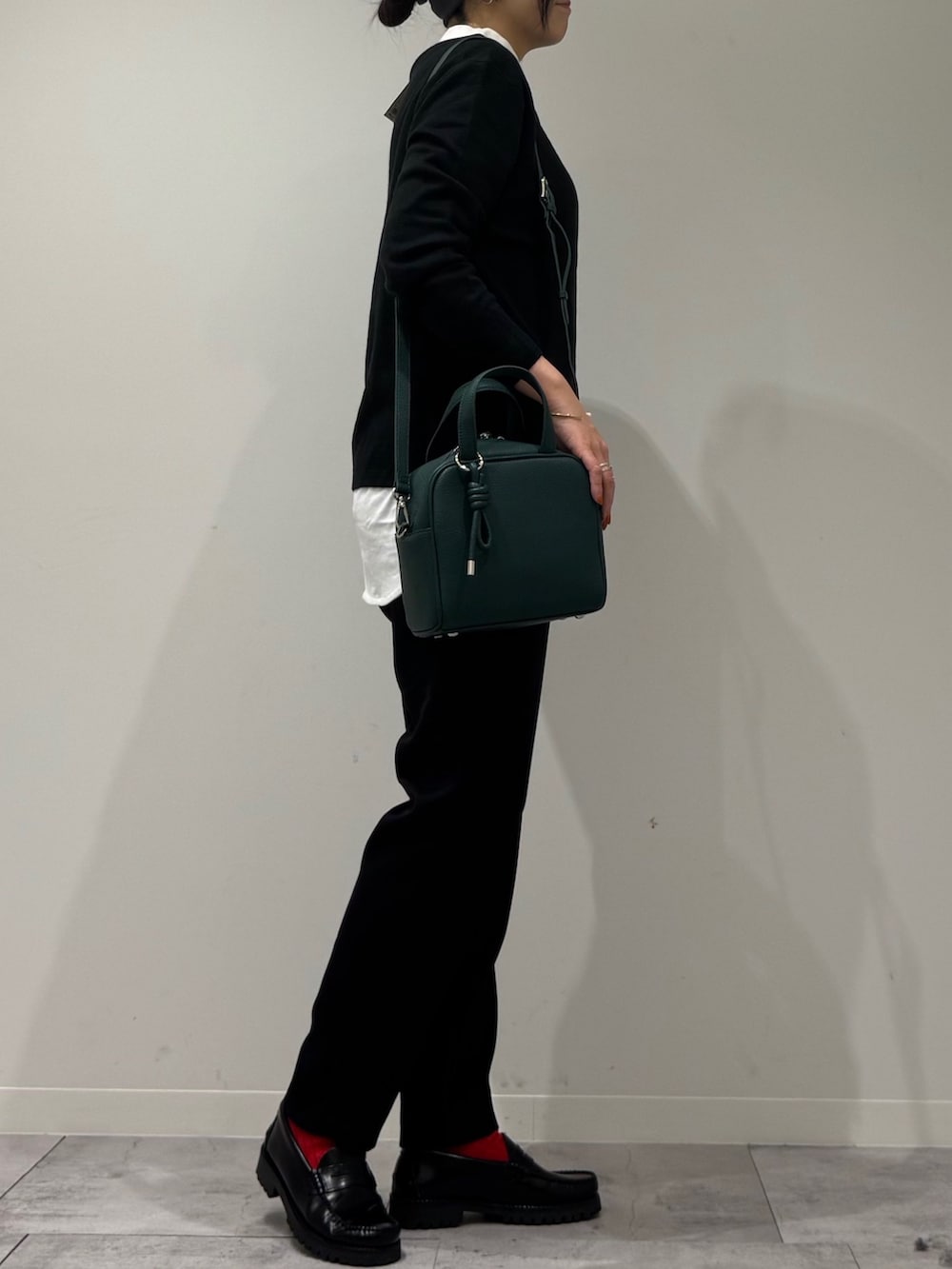 グリーン系のボストンバッグ、ブラック系のニット/セーター、ホワイト系のTシャツ/カットソーを着用したレディースの冬コーディネートの2枚目の写真
