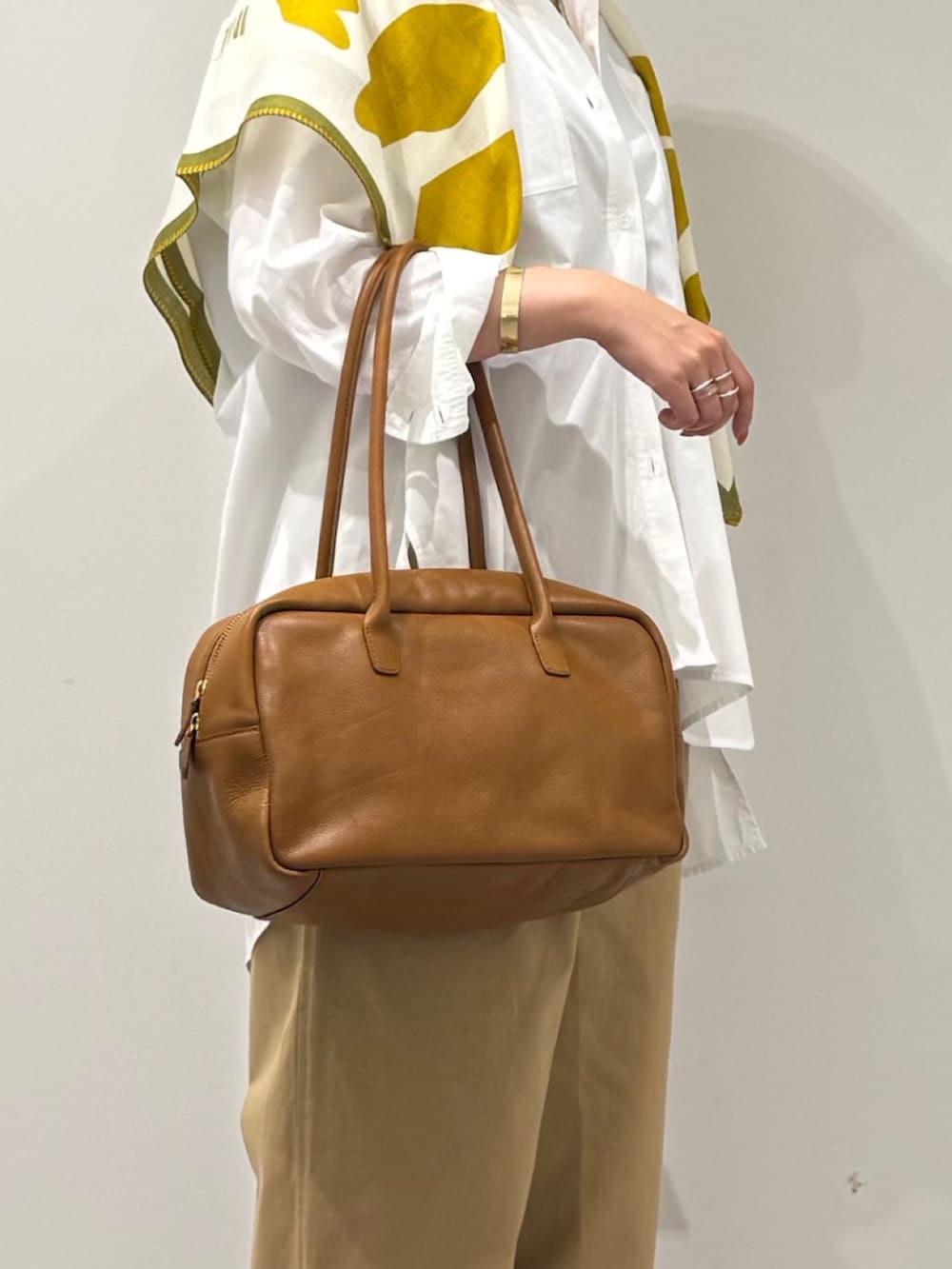 イエロー系のボストンバッグ、ベージュ系のチノパンツ、ゴールド系のバングル/リストバンドを着用したレディースの秋コーディネートの7枚目の写真